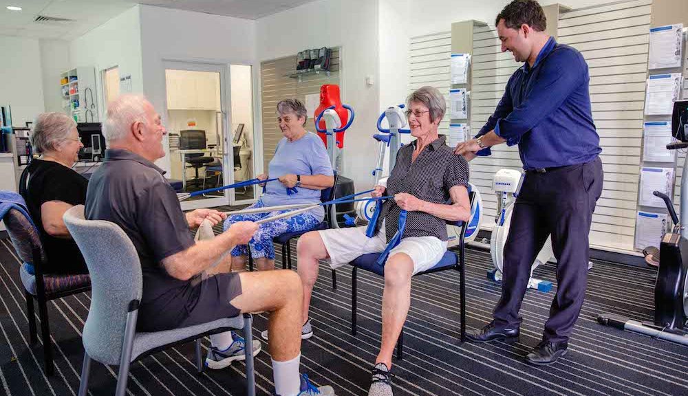 Elderly clients using resistance bands in pairs in UQ Health Care gym with exercise physiologist