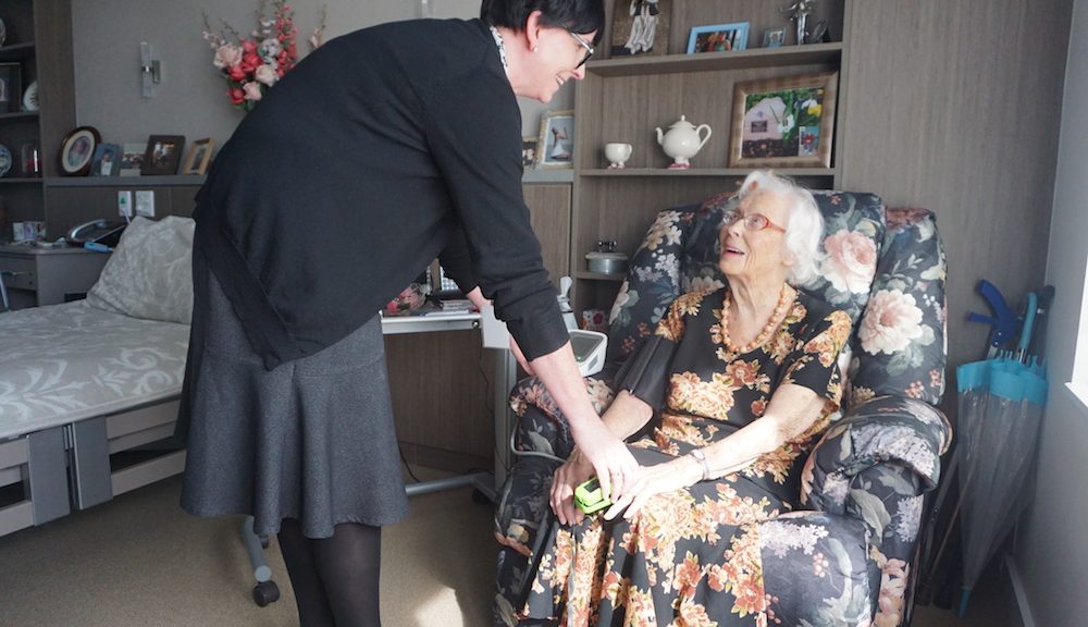 Nurse doing a home visit with elderly woman sitting in arm chair